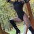 Woman posing on a wooden outdoor frame, wearing a black long-sleeve bodysuit, patterned fishnet tights, knee-high black boots, and a red hat. Woman posing on a wooden outdoor frame, wearing a black long-sleeve bodysuit, patterned fishnet tights, knee-high black boots, and a red hat.
